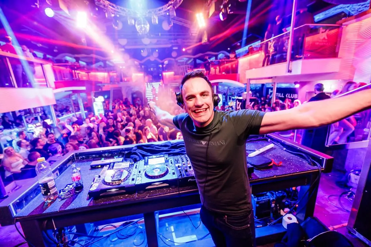 DJ Alex Cortez mit Kopfhörern am Pult, hinter ihm eine volle Tanzfläche